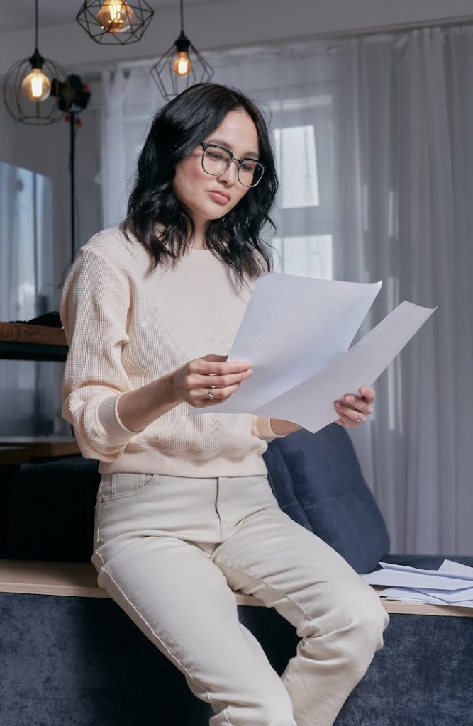 woman-in-white-sweater-holding-white-printer-paper-6963021 Thoughtful woman analyzing papers while seated indoors, reflecting on finance or work.